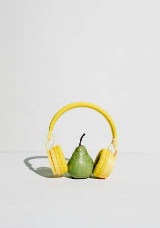 The music player in the shape of an pear with headphones. Fantasy on the theme of music and fruits, podcast for a healthy lifestyleの写真素材