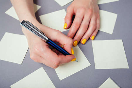 Yellow notes on a gray background and woman hand with pen