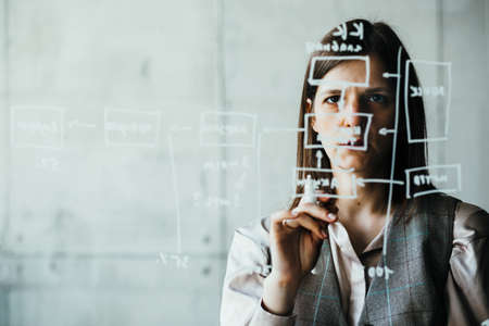 A woman writes with a white marker on a transparent board, user experience designerの写真素材