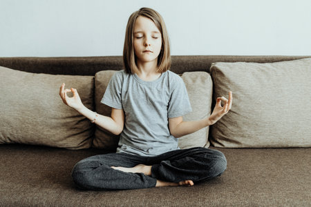 The girl is sitting at home on the sofa, yoga in the lotus position. Relaxation and tranquilityの写真素材