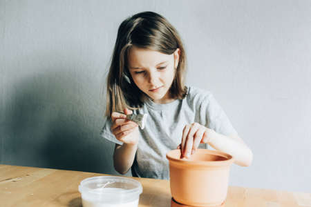 Girl paints a flower pot with white paint, hobby and decorative workの写真素材