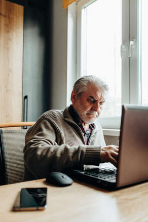 An elderly man works at a laptop, learning from home, home bookkeepingの写真素材