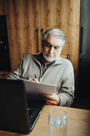 An elderly man works at a laptop, learning from home, home bookkeepingの写真素材