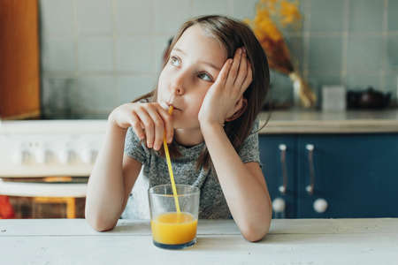 Girl thoughtfully drinking orange juice for breakfast, leisurely morning of school holidaysの写真素材