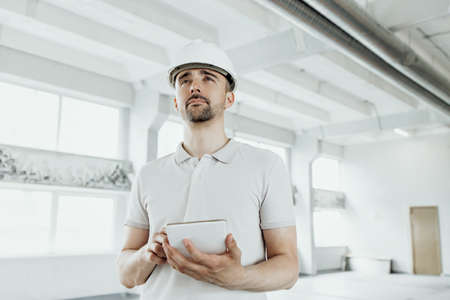 A man in a construction helmet on a counter checks a project on a tabletの写真素材