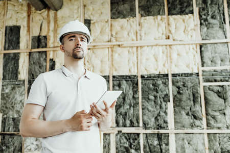 A man in a construction helmet on a counter checks a project on a tablet