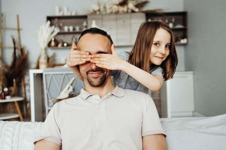 The girl closes her father's eyes and prepares a surprise for her father for the holidayの写真素材