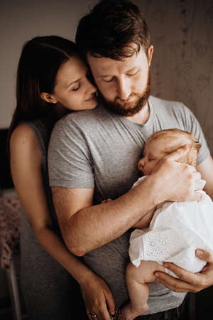 Father and mother holds baby in his arms standing at the window