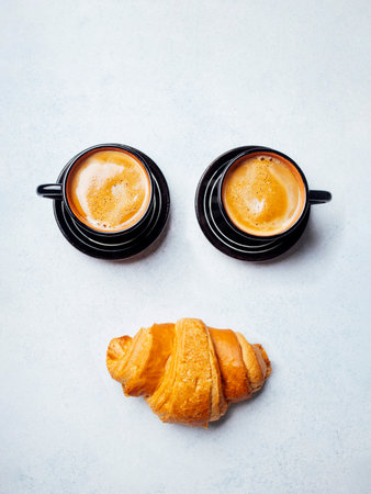 Two cups of coffee and a fresh croissant on the white tableの写真素材