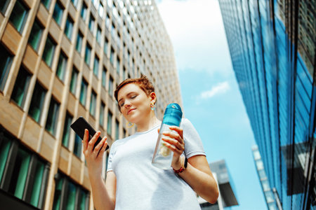 A young woman with a phone and a drink, outdoors in the summer in the city center