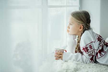 The girl at home looks at the snowfall, warm cozy day at home with teaの写真素材