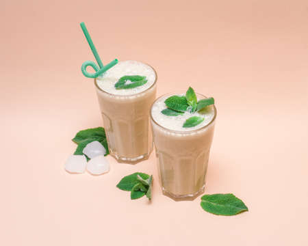 two glasses of refreshing smoothie with mint and ice around. cream backgroundの写真素材