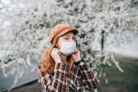 red hair girl in face mask standing in a flowering garden.の写真素材