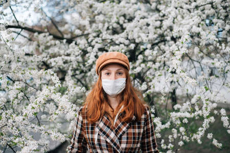 red hair girl in face mask standing in a flowering gardenの写真素材