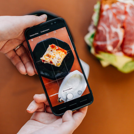 female hands hold a phone that photographs a toasted sandwich and yogurtの写真素材