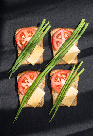 four slices of toast bread on a black tablecloth on each of which are feathers of onions, a slice of...