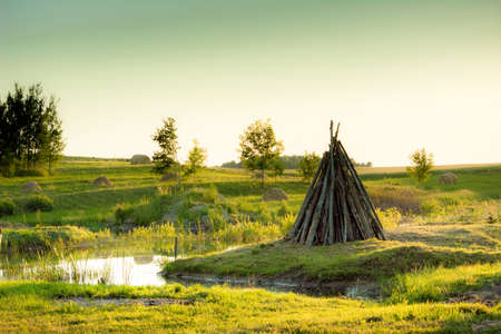 bright green bank of the river in the sunset light on which there is a fire prepared for setting fireの写真素材