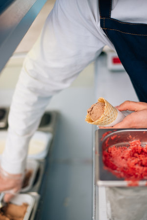 Waffle cone with delicious strawberry ice-cream in the hand. The seller puts a ball of ice-cream in a waffle cone by scoop or spoonの写真素材