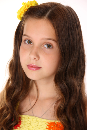 Portrait of a pretty young teenage girl close-up. Adorable preteen with dark hair, charming face and bare shoulders on a white background. The image of children's summer fashion.の写真素材