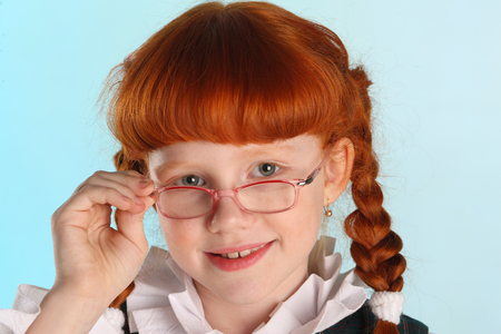 Close-up portrait of beautiful little redhead girl in a school uniform. Pretty attractive child posing with glasses. The young schoolgirl is 8 years old.の写真素材