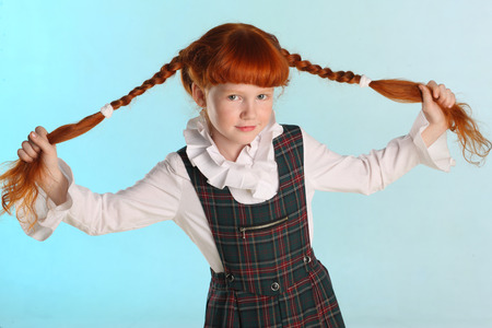 Portrait of beautiful little redhead girl shows her long chic hair. Cheerful attractive child-model in a school uniform. The young schoolgirl is 8 years old.の写真素材