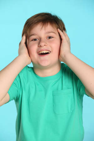 In this portrait, a handsome, cheerful young teenage boy hugs his head with joy and looks happily eye to eye.の写真素材