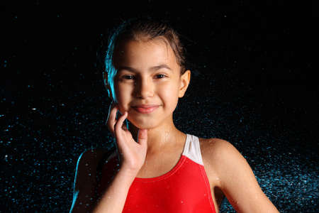 Close-up portrait of a beautiful teenage girl against the background of splashes of night rain, she touches her face with her hand and looks eye to eye.の写真素材