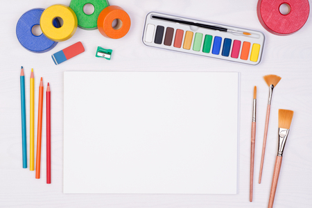 Blank piece of paper with colorful pencils, brushes and watercolors on kid's desk, top view with copy spaceの写真素材