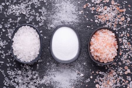 Various kinds of salt in black bowls on black stone background, top viewの写真素材