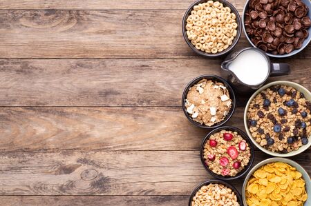 Breakfast cereals in bowls with a jug of milk on rustic wooden table, top view with copy space