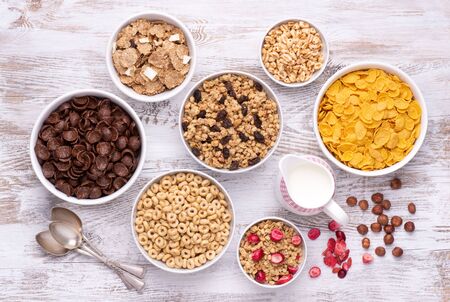 Breakfast cereals in white bowls on white wooden table, top view