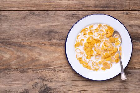 Cornflakes on a white enamel plate with milk on rustic wooden table, top view with copy spaceの写真素材
