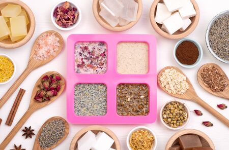 Soap mold and homemade soap ingredients. Five kinds of glycerin soap bases in wooden bowls and wooden spoons with dry herbs on white wooden backgroundの写真素材