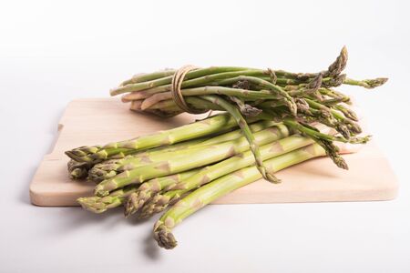 wild asparagus on a wood board prepared for cooking on a white backgroundの写真素材