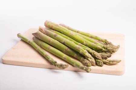 wild asparagus on a wood board prepared for cooking on a white backgroundの写真素材