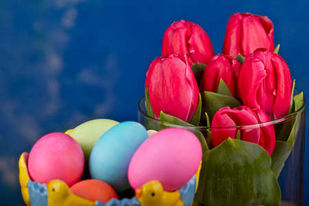 Tulips on vase and Easter colored eggs on blue background