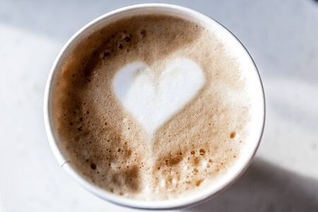Coffee latte in a plastic mug, artistic heart pattern on top
