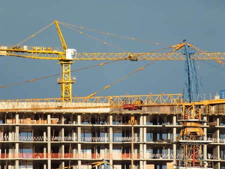 Two construction cranes with an uncompleted building