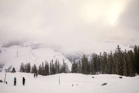 Snowy mountain landscape with people walking on a cloudy dayの写真素材