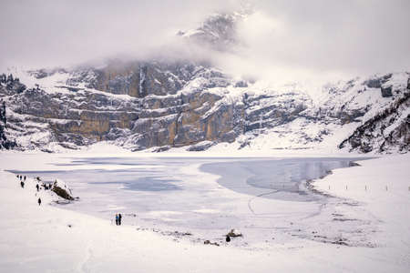 People spending day by frozen lake in snowy mountain landscape on a cloudy day in Switzerlandの写真素材