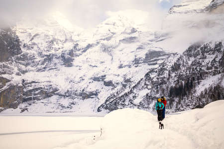 Couple walking their dog on a frozen lake in a snowy mountain landscape on a cloudy day in Switzerlandの写真素材