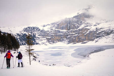 People walking along frozen lake in snowy mountain landscape on a cloudy day in Switzerlandの写真素材