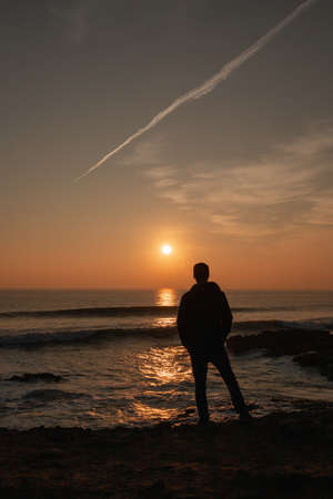 Man looking at the sunset in the Atlantic ocean in Portugal on a sunny day