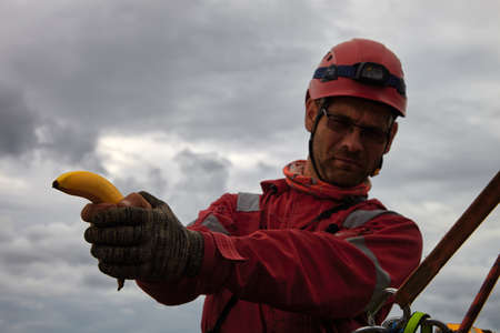 The banana is in focus in the hands of an installer in safety gear, and a protective helmet.