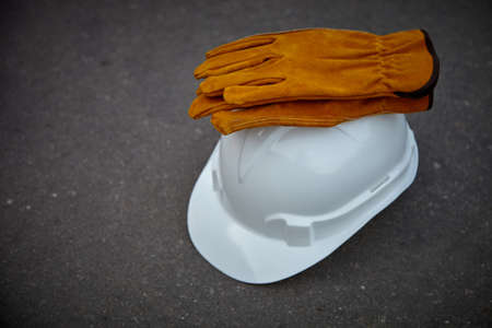 The construction helmet is white. Leather work gloves are on the helmet. The helmet and gloves are lying on the asphalt.の写真素材