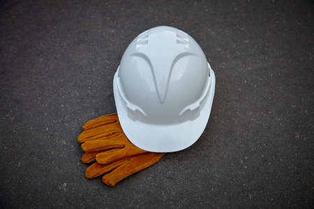 White paint and leather work gloves on a dark background. White construction helmet and leather gloves.の写真素材