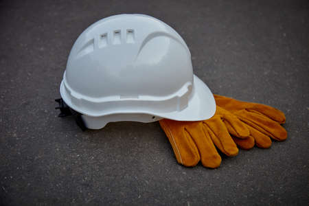 White paint and leather work gloves on a dark background. White construction helmet and leather gloves.の写真素材