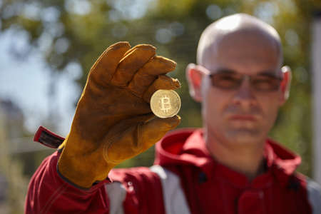Bitcoin coin in the hand of a working man.