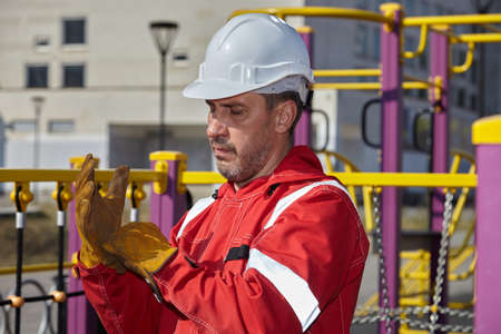 A man in a red work suit repairs a playground. A worker repairs a playground.