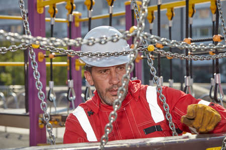 A man in a red work suit repairs a playground. A worker repairs a playground.の写真素材
